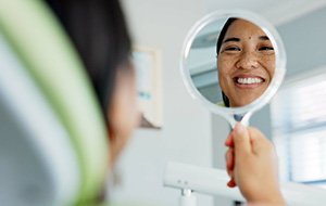 Woman smiling at reflection in handheld mirror